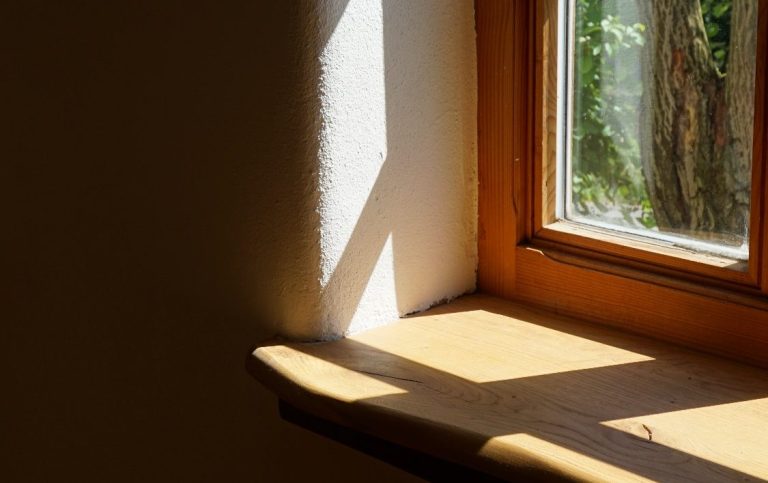 Ein helles Fenster mit Holzrahmen, das Schatten auf eine Fensterbank wirft.