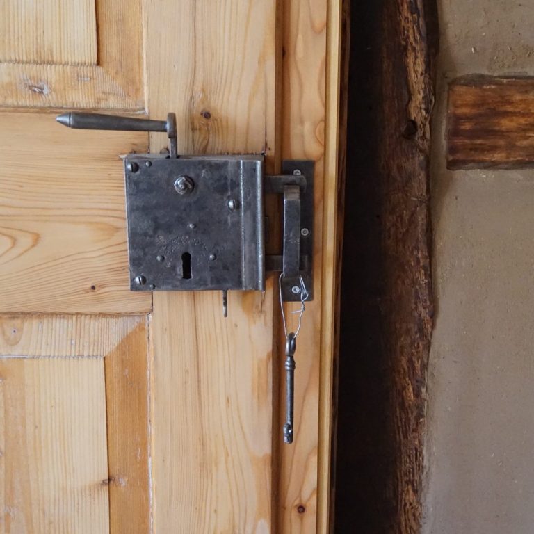 Alter, silberner Türschlossmechanismus an einer Holz Tür mit angrenzender Fachwerkwand und Lehmputz.