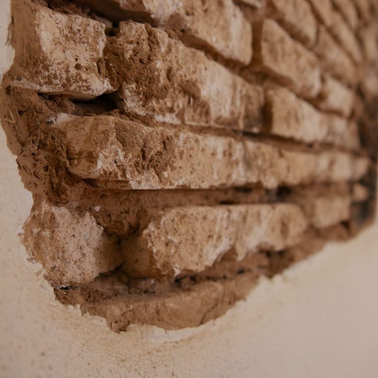 Nahaufnahme von einer unregelmäßigen, teils freiliegenden Lehmsteinwand.