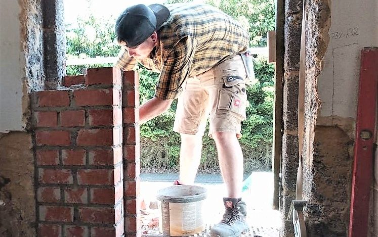 Person mauert Ziegelsteine auf einer Baustelle.