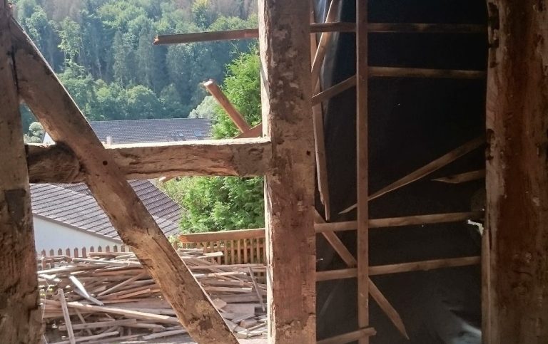 Blick durch einen Holzrahmen auf eine grüne Landschaft und Baustellenmaterialien.